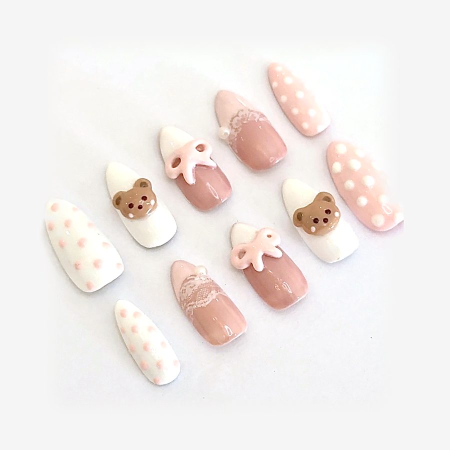 A press on nail set in white and blush pink with polka dots, lace tips, little bows and teddy bear charms